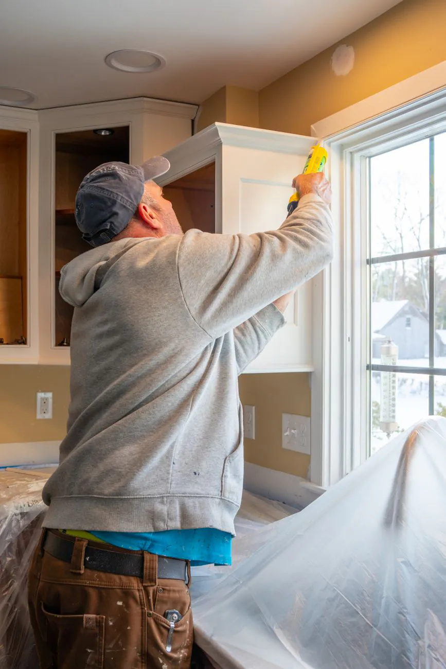 Man caulking kitchen cabinet during home renovation in Quincy, Massachusetts, USA.