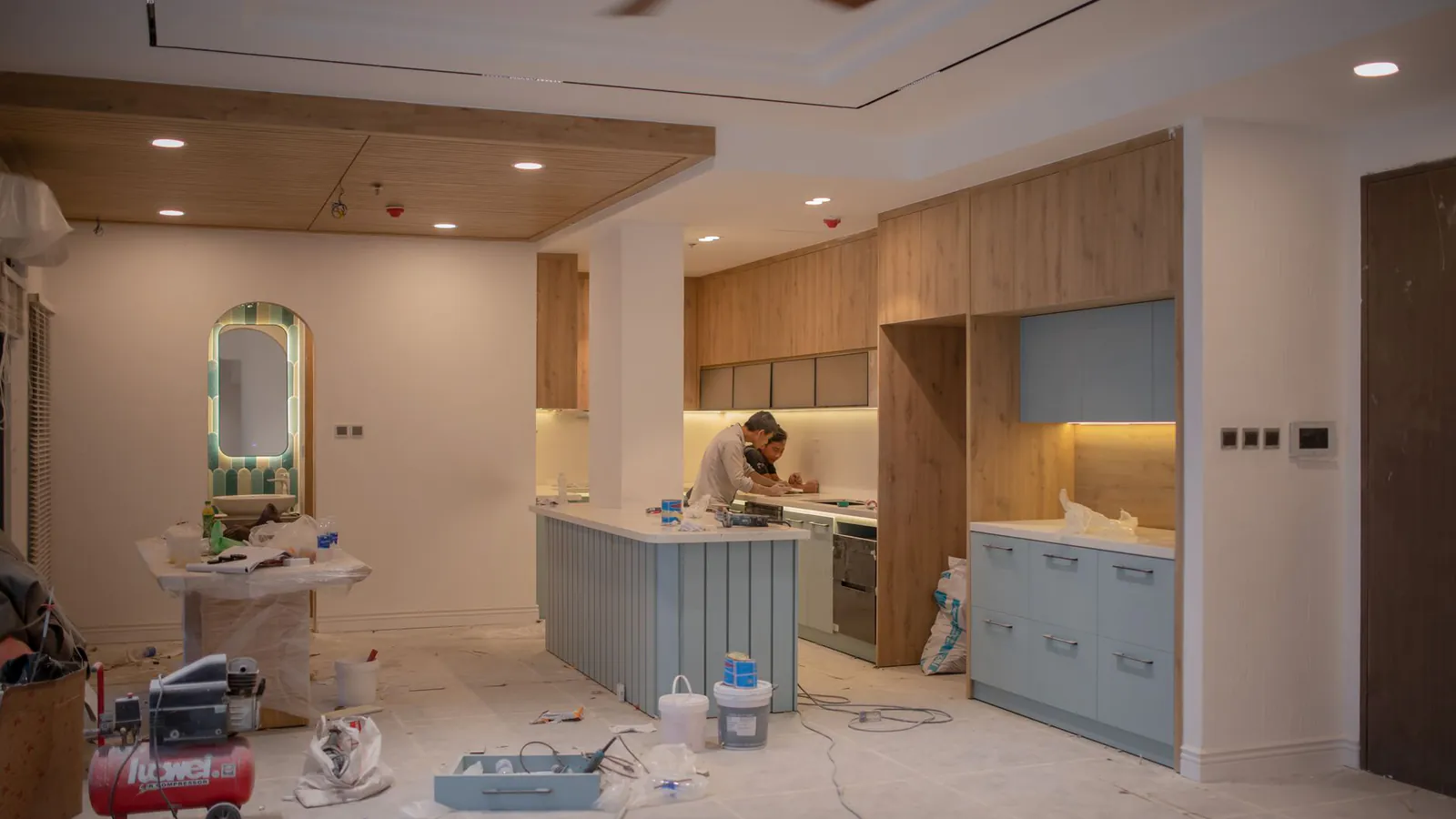 A modern kitchen undergoing renovation, featuring a worker, tools, and materials.
